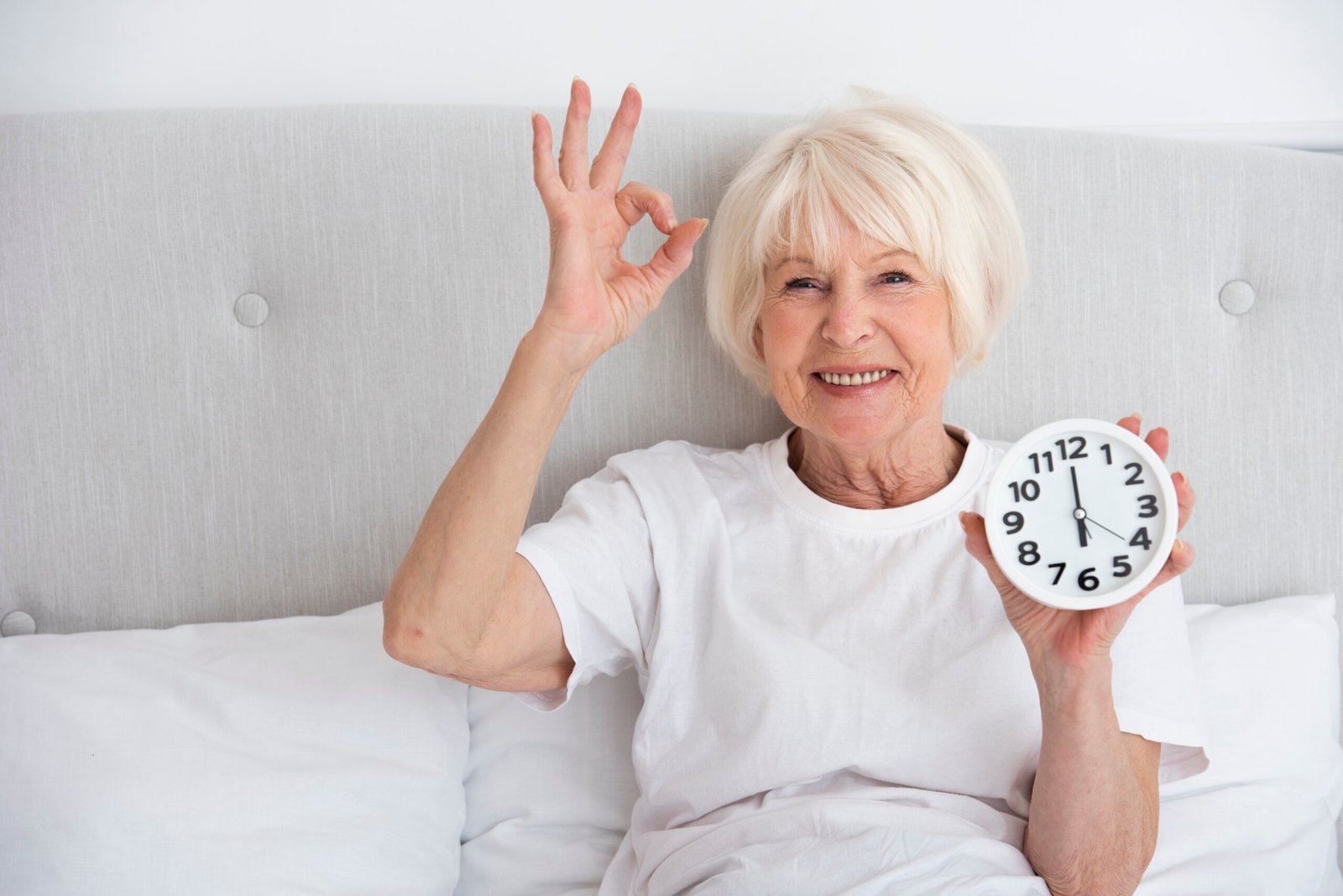Home happy elder woman holding clock her bed
